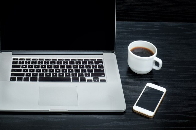 Foto abra o laptop, a caneca de café e o smartphone em um fundo preto