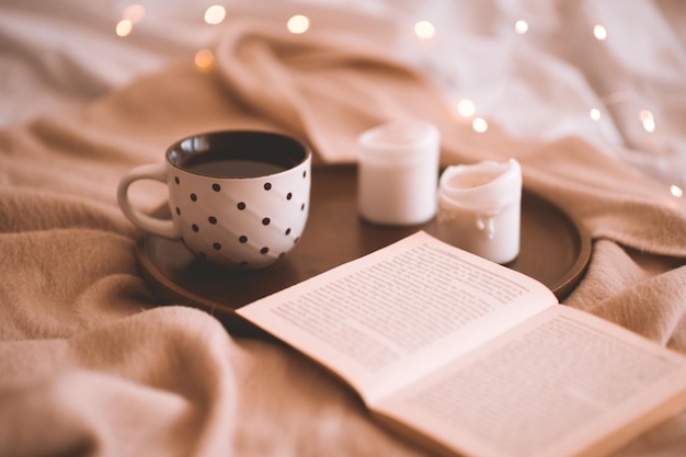 Abra o livro com uma xícara de chá e velas em pano de malha na cama closeup. Bom Dia. Hora do café da manhã. Estação do outono.