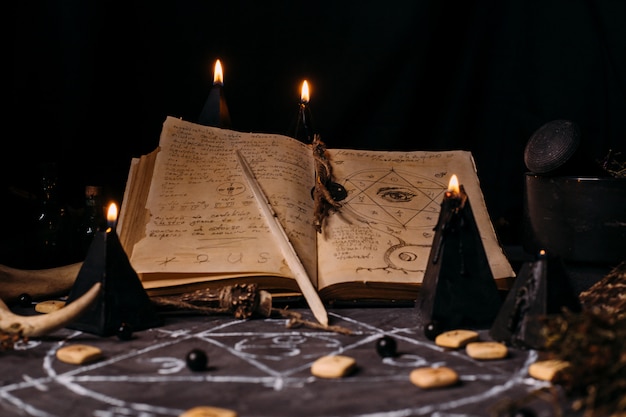 Abra o livro velho com feitiços, runas, velas negras na mesa de bruxa. Conceito oculto, esotérico, adivinhação e wicca. Cena do dia das bruxas