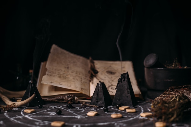 Abra o livro velho com feitiços, runas, velas negras na mesa de bruxa. Conceito oculto, esotérico, adivinhação e wicca. Cena do dia das bruxas