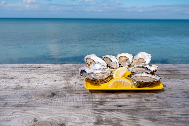 Abra ostras na placa amarela com limão no fundo do mar. Deliciosos frutos do mar, ostras frescas com limão na costa do mar.