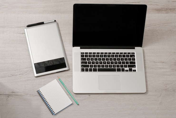 Foto abra el portátil, la tableta gráfica y el cuaderno con un lápiz sobre una mesa de luz, vista superior