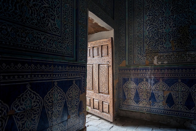 Abra la puerta de madera tallada al cuarto oscuro con adornos excepcionales en azulejos de mayólica Khiva Uzbekistán