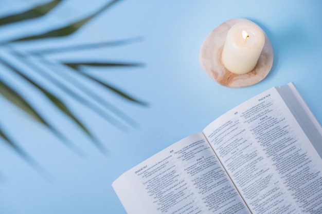 Abra la Santa Biblia con velas y hojas de palma sobre fondo azul.