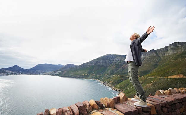 Abraçando a magnificência da natureza Foto de um jovem de pé em uma parede olhando para o cenário natural