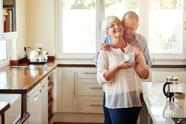 Abraçando café ou casal de velhos rindo na cozinha em casa se unindo ou aproveitando o tempo de qualidade juntos Abrace a aposentadoria ou um homem maduro feliz conversando relaxando ou bebendo chá com uma mulher sênior engraçada