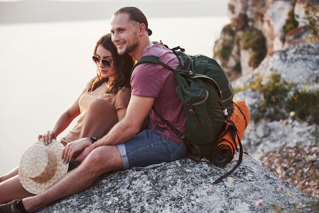 Abraçando o casal com mochila, sentado no topo da montanha de pedra, apreciando a vista costa um rio ou lago. viajar ao longo de montanhas e costa, liberdade e conceito de estilo de vida ativo