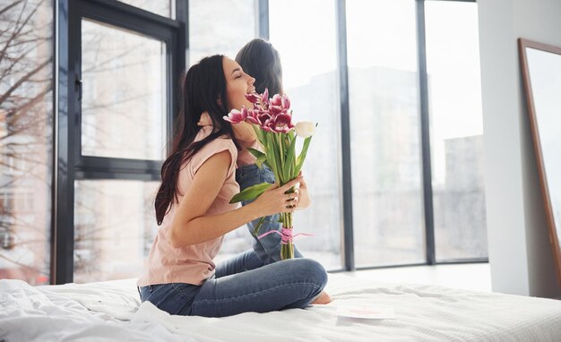 Abraçando-se Filha felicita mãe com feriado e dá buquê de flores