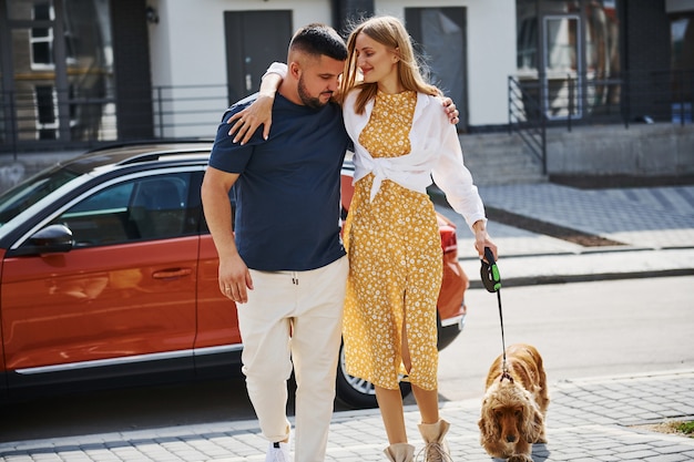 Abraçando-se. lindo casal passear com o cachorro ao ar livre perto do carro.