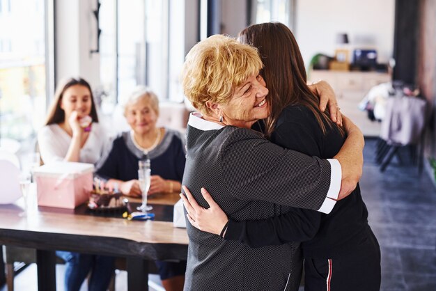 Abraçando-se. Mulher sênior com família e amigos comemorando um aniversário dentro de casa.