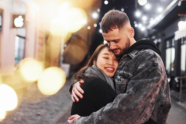 Abraçando um ao outro Feliz casal multirracial juntos ao ar livre na cidade comemorando o ano novo