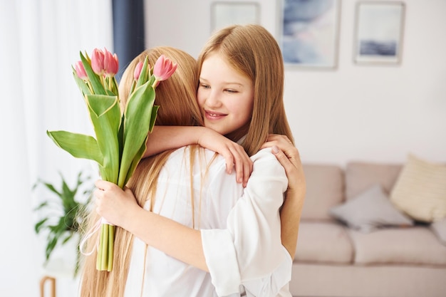 Abraçando uns aos outros Jovem mãe com sua filha está em casa durante o dia