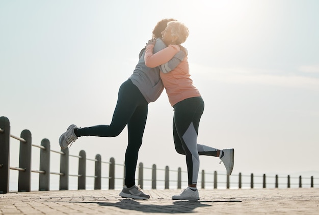 Abraço de corrida e mulheres pelo mar e oceano com amor e cuidado para fitness e exercício Bem-estar do atleta e amigas em um passeio de praia com abraço de motivação e sorriso do alvo do corredor