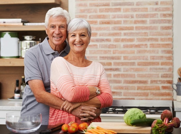 Abraço de cozinha e retrato de casal de velhos na cozinha para salada amor e nutrição Sorriso feliz e aposentadoria com homem e mulher sênior cortando legumes em casa para jantar de comida e receita