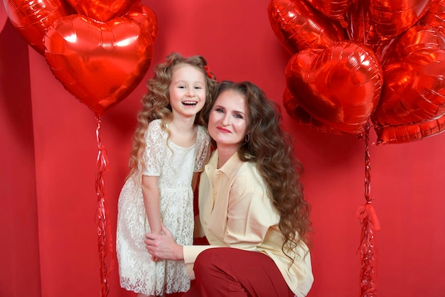 Abraço de menina linda com mãe mãe sorri em fundo vermelho com balão em forma de coração e uma caixa de presente O conceito de amor presente Dia dos Namorados 14 de fevereiro 8 de março dia das mães