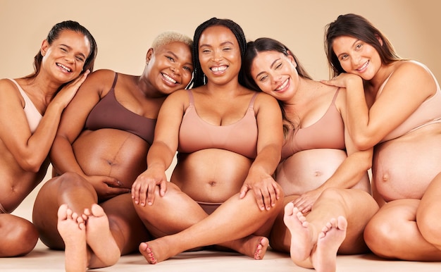 Abraço de retrato grávida ou mulheres sentadas em roupas íntimas para apoio à diversidade de vínculo comunitário ou empoderamento corporal Sorriso feliz chão ou amigos de gravidez em saúde, bem-estar, futuro bebê ou amor