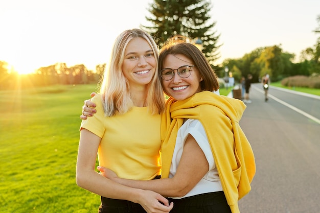 Abrazando a feliz madre sonriente e hija adolescente juntas. Retrato de familia en el parque, fondo del día soleado al atardecer. Día de la madre, dos generaciones, estilo de vida, amor y felicidad.