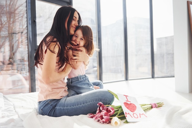 Abrazándose La hija felicita a la madre con las vacaciones y le da un ramo de flores.