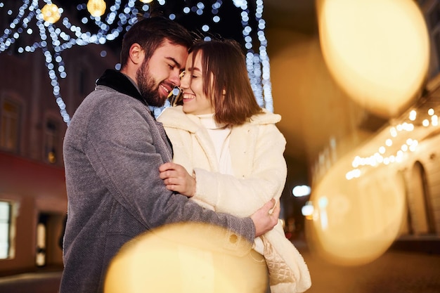 Abrazándose unos a otros Feliz pareja joven celebrando el Año Nuevo al aire libre en la calle