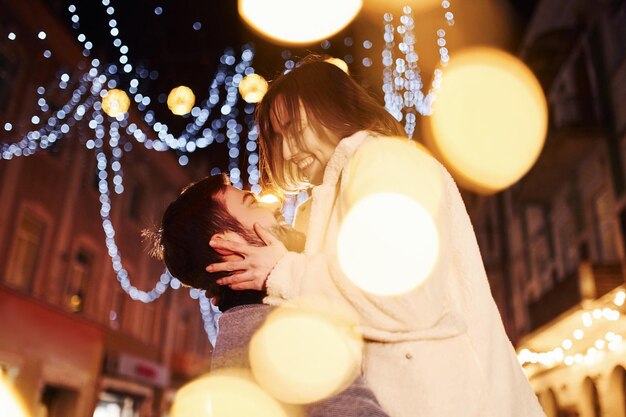 Abrazándose unos a otros Feliz pareja joven celebrando el Año Nuevo al aire libre en la calle