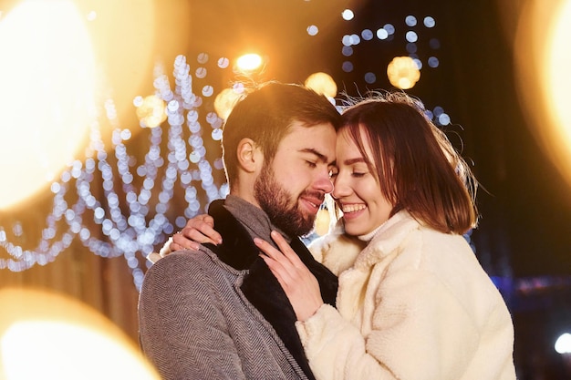 Abrazándose unos a otros Feliz pareja joven celebrando el Año Nuevo al aire libre en la calle