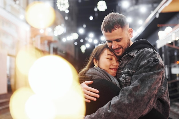 Abrazándose unos a otros Feliz pareja multirracial juntos al aire libre en la ciudad celebrando el Año Nuevo