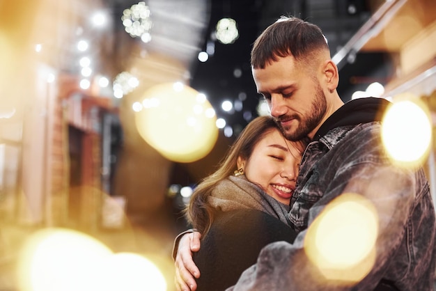 Abrazándose unos a otros Feliz pareja multirracial juntos al aire libre en la ciudad celebrando el Año Nuevo