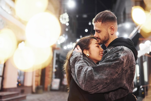 Abrazándose unos a otros Feliz pareja multirracial juntos al aire libre en la ciudad celebrando el Año Nuevo