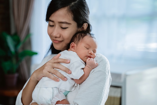 Abrazo asiático de la madre que lleva a la pequeña hija recién nacida