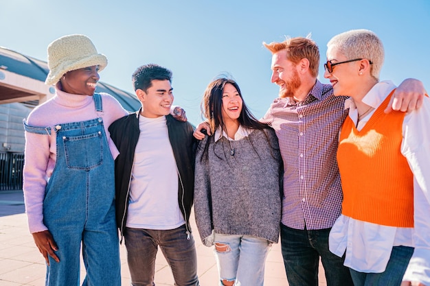 Abrazo en grupo de amigos multiculturales Cinco jóvenes disfrutando de un día soleado Adolescentes riendo y hablando con actitud positiva