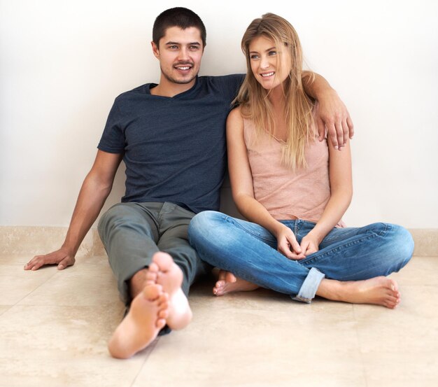 Foto abrazo, relajación y pareja en el piso de su nueva casa hablando de bonos y emocionados por el éxito inmobiliario mudanza de propiedad y hombre y mujer sentados juntos en el suelo de la sala de estar en la casa de sus sueños