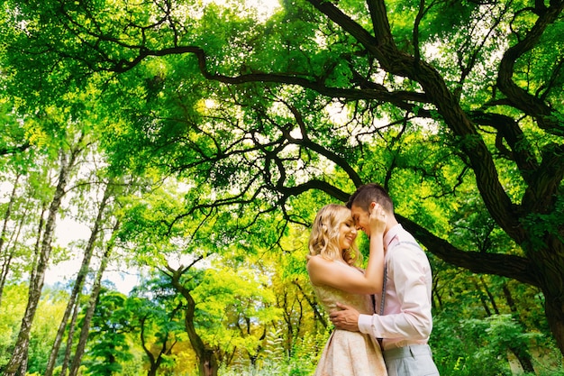 Abrazos sensuales de dos amantes de las personas en el fondo de árboles verdes