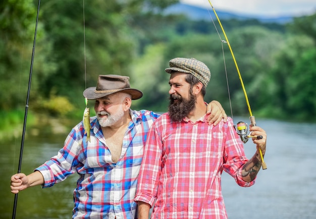 Los abrazos son totalmente retornables fin de semana de verano hombres maduros pescador amistad masculina unión familiar dos pescadores felices con cañas de pescar pasatiempo y actividad deportiva Cebo de trucha pesca de padre e hijo