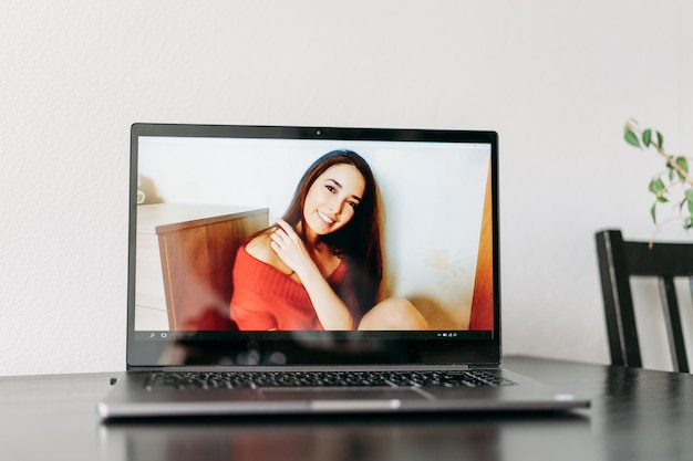 Abre una computadora portátil en la mesa con una foto de una chica asiática riendo en un vestido rojo de una sesión de fotos de una llamada de video