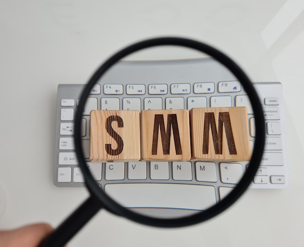 Abreviatura SMM de cubos de madeira no teclado de computador e lupa Marketing de mídia