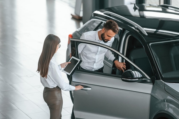 Foto abriendo la puerta el hombre con la mujer vestida de blanco están juntos en el concesionario de automóviles