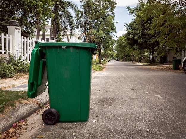 Abrió un gran cubo de basura de plástico verde vacío frente a la casa moderna con árboles verdes No hay basura pública al lado de la carretera Control infeccioso de eliminación de basura concepto de eliminación de residuos