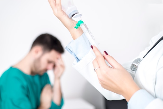 Foto abschluss herauf detailansicht an weiblichem doktor bereitet eine einspritzung vor, während der patient im bett ist