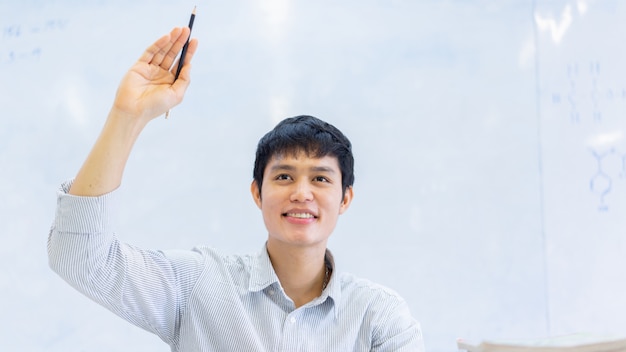 Abschluss herauf junge asiatische Hochschulstudenten-Mannerhöhungshand zum Fragen des Lehrers nach Projekt oder Prüfung im Klassenzimmer für Bildung und Leutekonzept