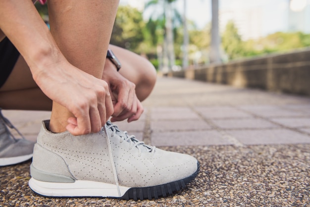 Abschluss oben der jungen Frau schnüren sich oben ihr Schuh, der zum Training auf dem Trainieren im Park bereit ist