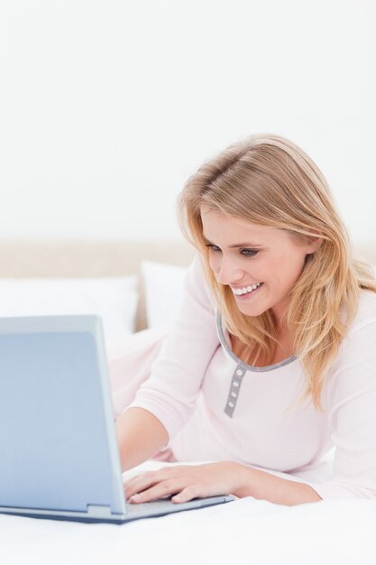 Foto abschluss oben, frau, die einen laptop während auf dem bett und dem lächeln verwendet