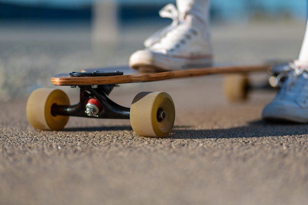 Abschluss oben von Damenbein in den weißen Turnschuhen, die nach extremer lustiger Fahrt ihr hölzernes longboard Skateboard, modernes städtisches Hippie-Mädchen stillstehen, haben Spaß, guten sonnigen Sommertag für das Skateboard fahren und haben Spaß