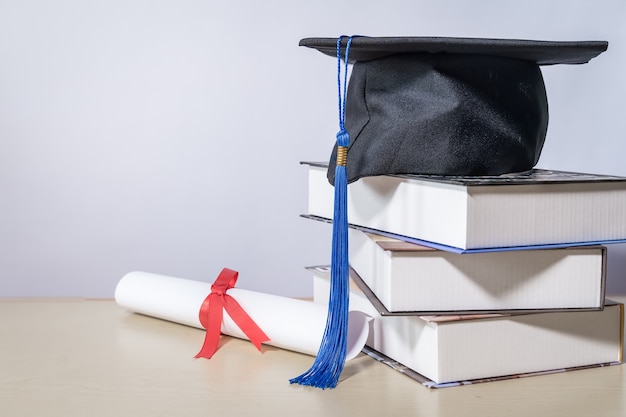 Abschlusshut mit Büchern und Diplom auf dem Tisch vor weißem Hintergrund