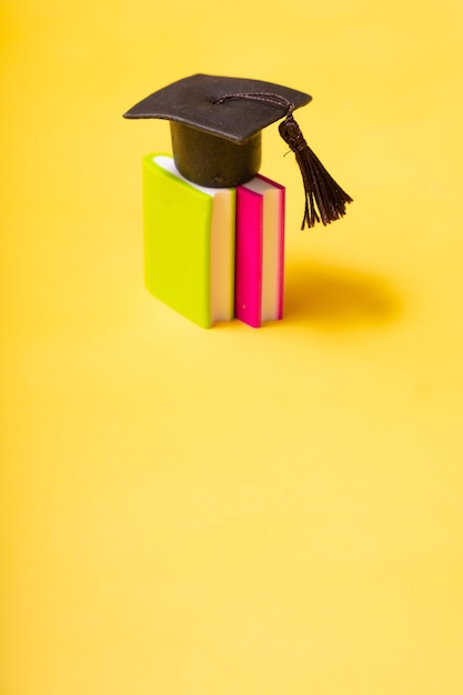 Abschlusskappe auf bunten Büchern auf gelbem Hintergrund Bildungskonzept mit Kopierbereich