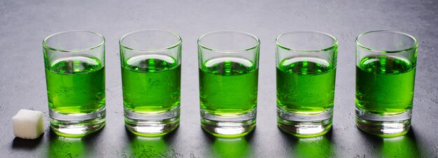 Absenta licor verde en vasos. Bebida alucinógena alcohólica. Fondo oscuro Pedazos de azucar blanca