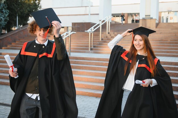 Absolventen in Mänteln mit Diplomen in den Händen stehen in der Nähe der Universität