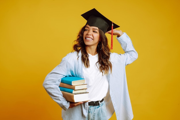 Absolventin in einem Abschlusshut auf ihrem Kopf, mit Büchern auf Gelb.