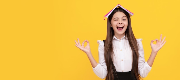 Absorbiendo el conocimiento Colegiala feliz sostenga el libro en la cabeza haciendo un gesto de mudra Día del conocimiento Retrato de colegiala estudiante estudio banner encabezado Escuela niño cara copyspace