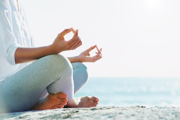 Absorbiendo la paz de la naturaleza Una mujer joven realizando una rutina de yoga en la playa bajo el sol de verano