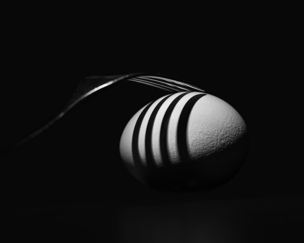 Abstracto preto e branco, imagem de natureza morta escura de ovo e garfo brilhantemente iluminados com sombras contrastantes